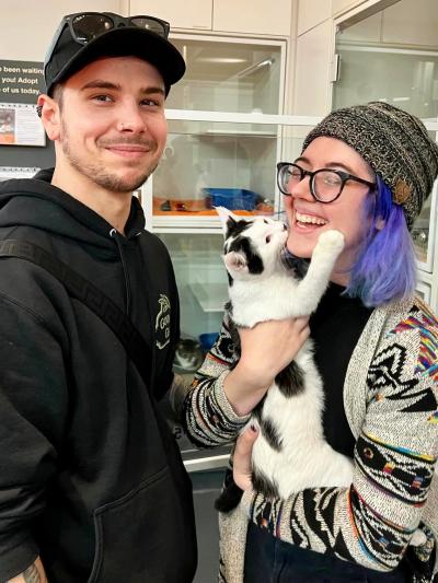 Berry the kitten face-to-face kissing his smiling and laughing adopter with the other adopter next to them