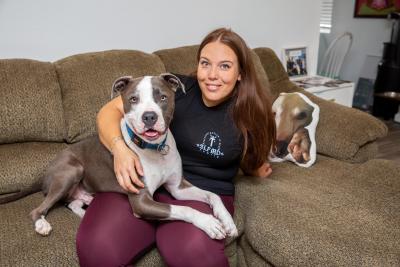 Smiling person on a couch with a pit bull type dog lying in her lap