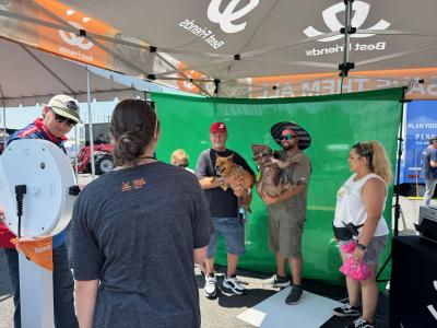 People holding dogs in front of a green screen in a Best Friends tent at Pocono Raceway