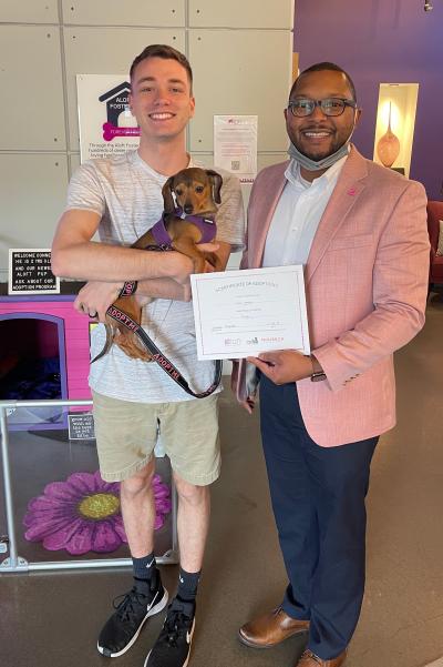 Two people holding a dog and an adoption certificate at the Aloft Hotel