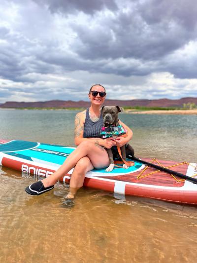 Angie with Pepper the dog sitting on a kayak at a reservoir of water