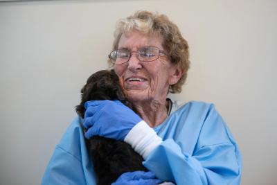 Betty the volunteer, wearing a protective gown and gloves, holding a puppy