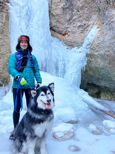 Kathleen and Koda the dog outside surrounded by an ice formation on a boulder