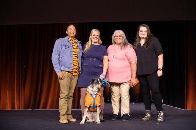 Omar, Talia, Janine, and Grace on the stage at the Best Friends National Conference with a dog