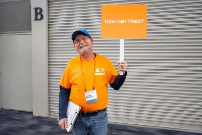 Smiling Best Friends National Conference volunteer wearing an orange T-shirt and holding a sign that says, 'How can I help?'