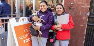 Woman in purple jacket holding small tan dog next to woman in white jacket holding a folder