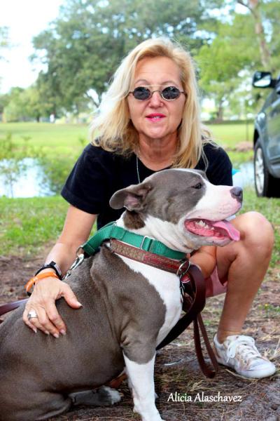 Smiling person wearing sunglasses with hand on the back of a gray and white pit-bull-type dog