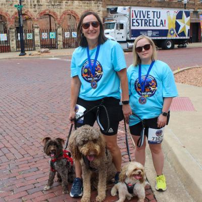 Two Bank in the Park attendees wearing medals around their necks with three dogs on leashes