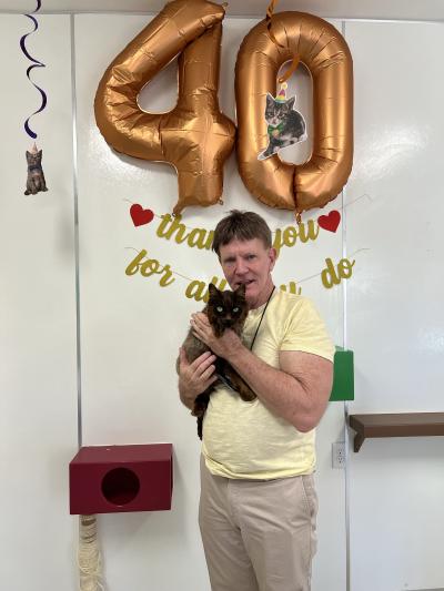 Volunteer Bill Coaker holding Pepe the cat below a large 40 balloon
