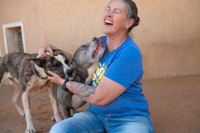 Laughing person petting a dog while another dog tries to lick her face.