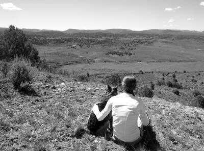 Black and white photo of Ashley with her arm around Cayenne the dog looking out over rolling hills