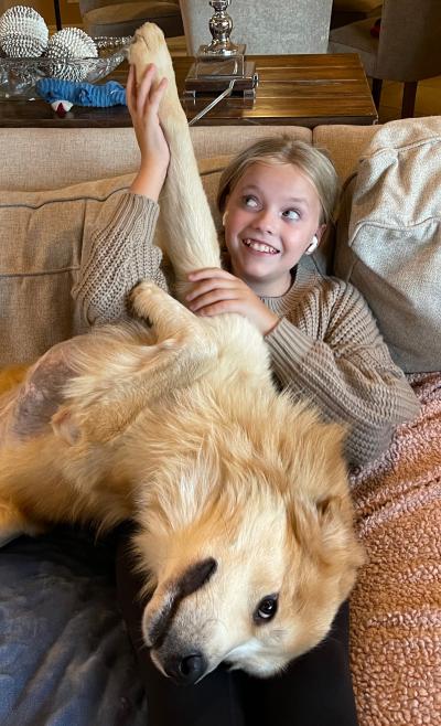 Caesar the dog lying upside down on a couch in a smiling person's lap with his front paw up in the air