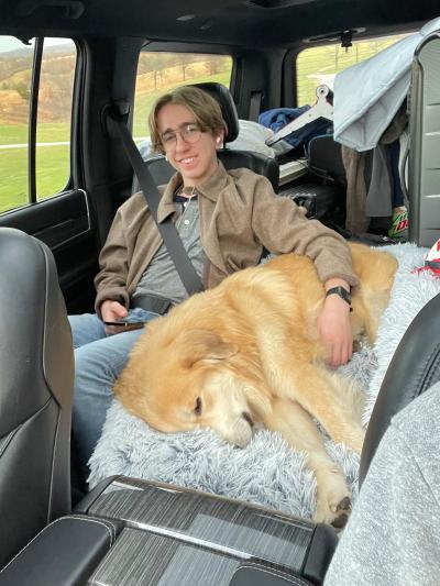 Caesar the dog sleeping on a fluffy blanket in a vehicle with a person next to him with his arm around him