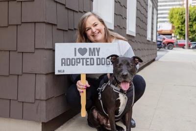 Jill Shaw holding a sign that reads "I heart my adopted dog" next to Captain the dog after adopting him