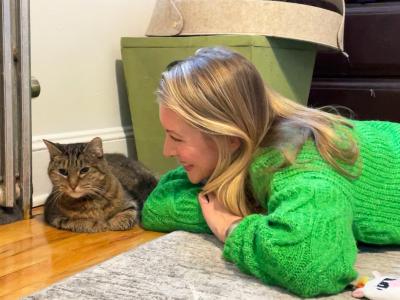 Nicole wearing a green sweater lying on the floor beside Suzie the cat