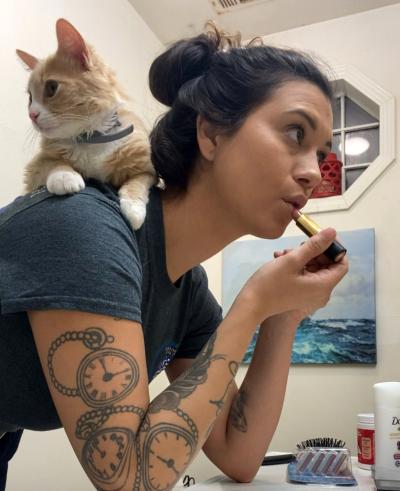 Tebow the cat sitting on his person's shoulders while she applies makeup