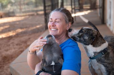 Person smiling and hugging a dog while Blanche looks over