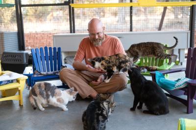Volunteer Curtis McIff sitting on the floor with cat surrounded by chairs he made