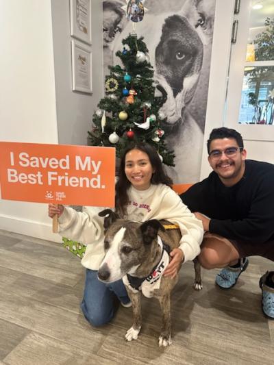 Dakota the dog on adoption day with his adopters, with one holding a Best Friends sign that says, "I saved my best friend"