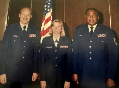 Denise Deisler in an Air Force uniform between two people in front of an American flag