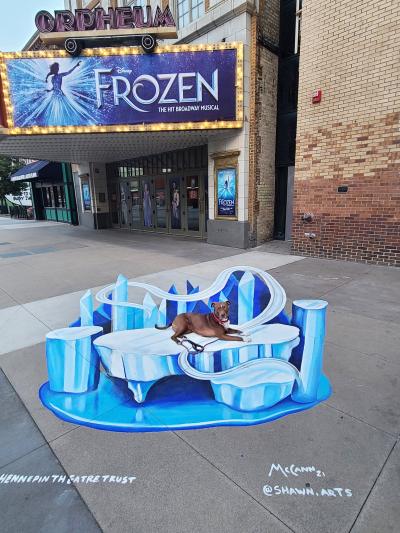 Dandelion the dog on a 'Frozen' display in front of a theatre sign promoting the show