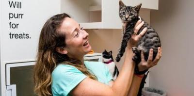 Woman in light teal shirt holding up a tabby kitten