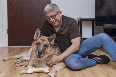 Person lying on the floor next to a senior dog with a toy