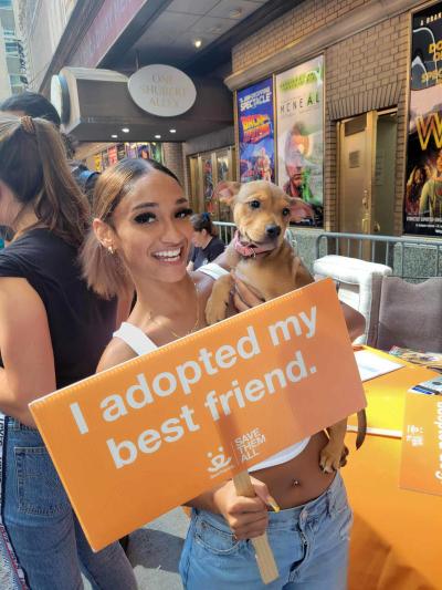 Noemi Peguero holding the dog she adopted with a sign that says, I adopted my best friend