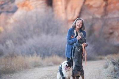 Best Friends co-founder Faith Maloney in Angel Canyon walking two dogs, one who has jumped up on her and she's laughing
