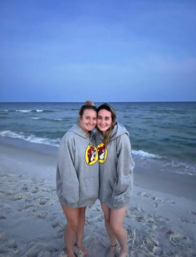 Volunteers Lauren Burgess and Jill Church on a beach together wearing matching Buckee's sweatshirts