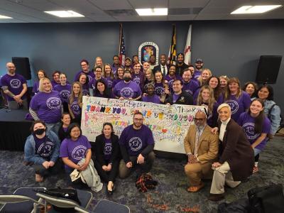Large group of people wearing purple Pet Unity Project T-shirts around a sign thanking Chair Burrough