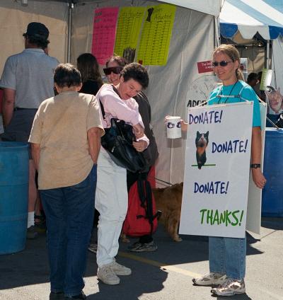 Julie Castle soliciting donations in a coffee can wearing a sign that says, 'Donate! Donate! Donate! Thanks!'
