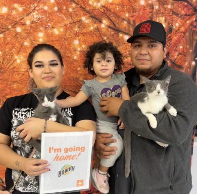 Emillo and Perry the cats being held by the two people in their new family with a toddler with one person holding a paper that says, 'I'm going home!' with the Bounty logo