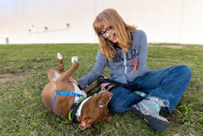 Holly Sizemore sitting on some grass laughing and petting a dog's belly