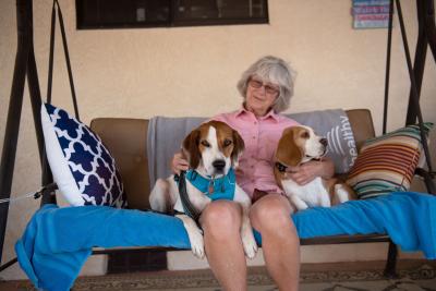 Elvis and another dog sitting on either side of Mary on a porch swing