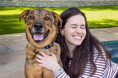 Person hugging a brown dog who is smiling