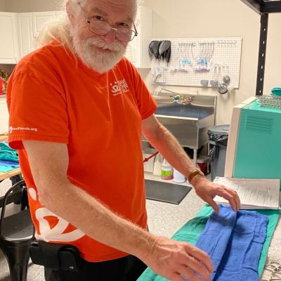 Volunteer Bob Burleson wearing an orange Best Friends T-shirt with a blue cloth in front of him from an instrument pack