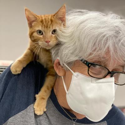 Volunteer Maggie Schroeder wearing a mask with an orange kitten on her shoulder