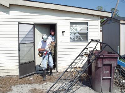 Person carrying a rescued Chihuahua mix dog out of a home after Hurricane Katrina