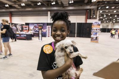 Young person holding a small white dog and wearing an orange Best Friends 'I saved a life' sticker 