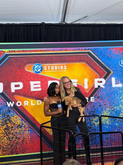 Best Friends CEO Julie Castle holding a puppy beside another person holding a microphone at the SUPERGIRL world premiere