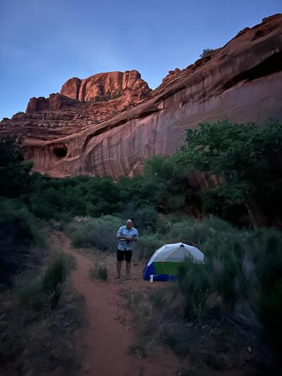 A campsite in a canyon below a large red cliff in the evening