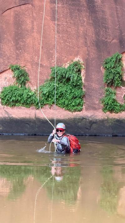 Julie Castle in water holding rappel ropes beside a rock wall