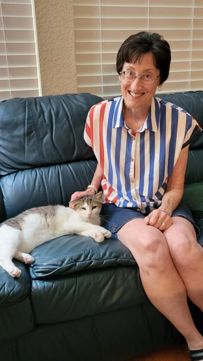 Ann Butchello sitting on a couch beside Buddy the cat petting him