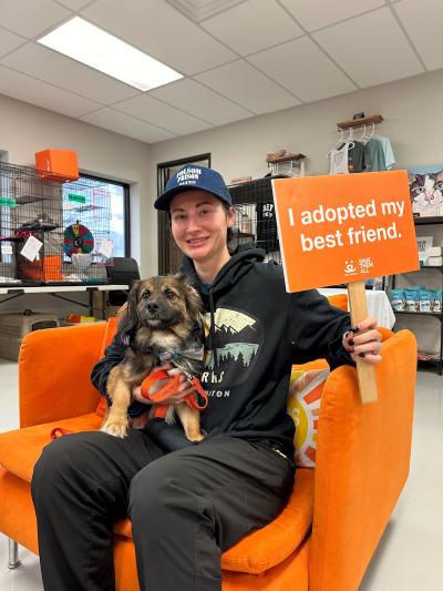 Mackenzie Wilhite with Nikki the dog on her lap while holding a sign that says, 'I adopted my best friend'