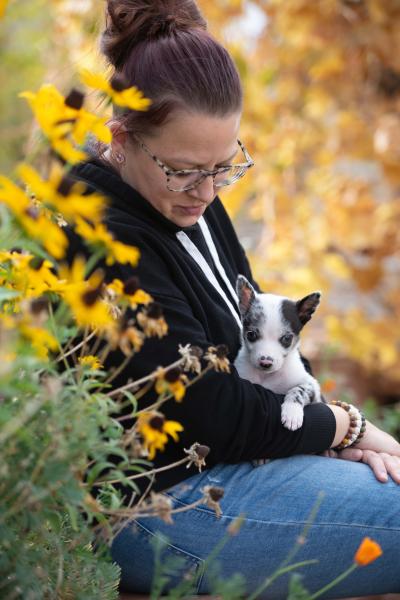 Jessica holding Polly Pocket the puppy in her lap beside some yellow flowers