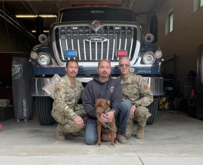 Zap the dog with three people in military clothing in front of a large truck