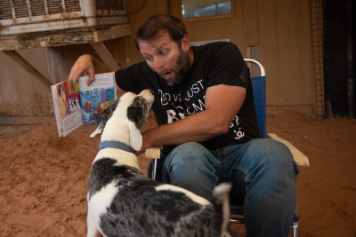 Jonathan Hudson the caregiver making a face while reading a book to Frankie the deaf dog