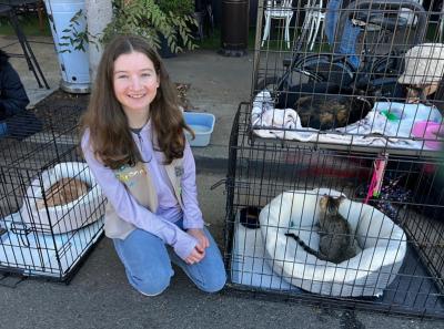 Ariela kneeling next to some wire kennels containing cats
