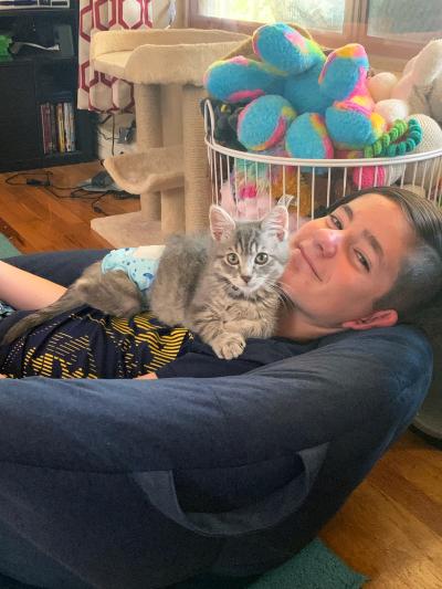 Kelsi holding Benedict the kitten on her chest while sitting in a chair